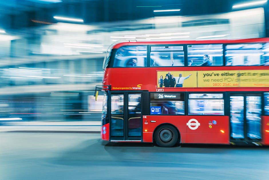 An aerial black-and-white photograph showing a busy suburban area with residential houses and streets in Thamesmead, SE28. The image features a major multi-lane road running vertically through the scene, with several vehicles including trucks and cars traveling along it. Over this main road, a smaller bridge or overpass crosses, supported by concrete pillars, facilitating the movement of traffic above the lower road. Adjacent to the road are railway tracks with electrical wiring and pylons running parallel, indicating the proximity of rail transport to the residential zones. Surrounding the roads are numerous houses, many with pitched roofs, gardens, and trees, typical of a suburban neighbourhood. The area appears well-developed with a mixture of commercial and residential buildings, and the lighting suggests daytime conditions. This setting exemplifies urban and suburban infrastructure, relevant to house removals and moving logistics, where careful planning of transport routes is essential, which [COMPANY_NAME], Man with Van Thamesmead, can assist with during home relocation or furniture transport services.