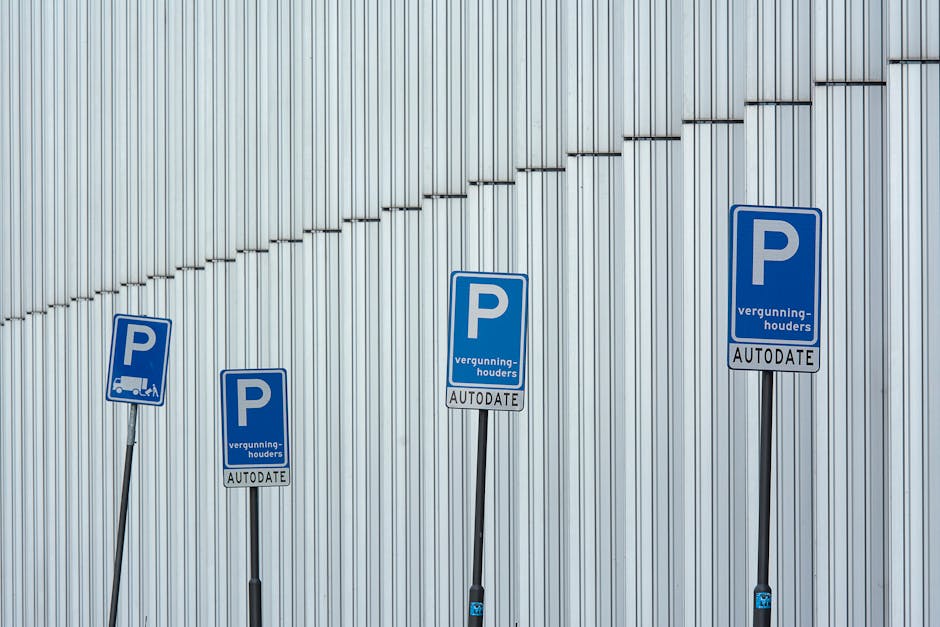 Four blue parking signs with white 'P' symbols and the words 'vergunning-houders AUTODETE' are mounted on black metal posts in front of a modern, vertically paneled metallic wall. The signs are evenly spaced at different heights, with the tallest on the right and the shortest on the left. The scene is illuminated by natural light, casting soft shadows. This image is linked to house removals and moving logistics, illustrating parking regulations for vehicle access during a home relocation or furniture transport process, as handled by Man with Van Thamesmead, which often requires understanding parking permits or suspensions for efficient move planning.